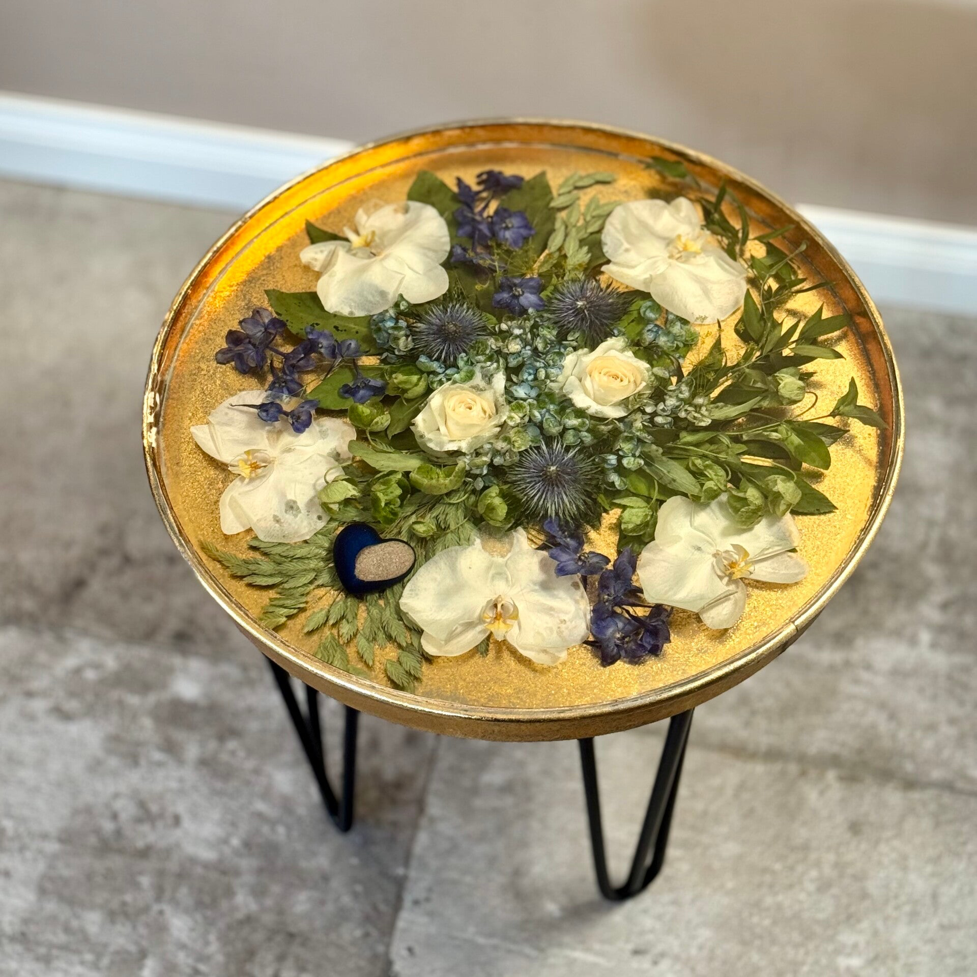 Rouwbloemen verwerkt in gouden tafel met blauw hartje gevuld met as.