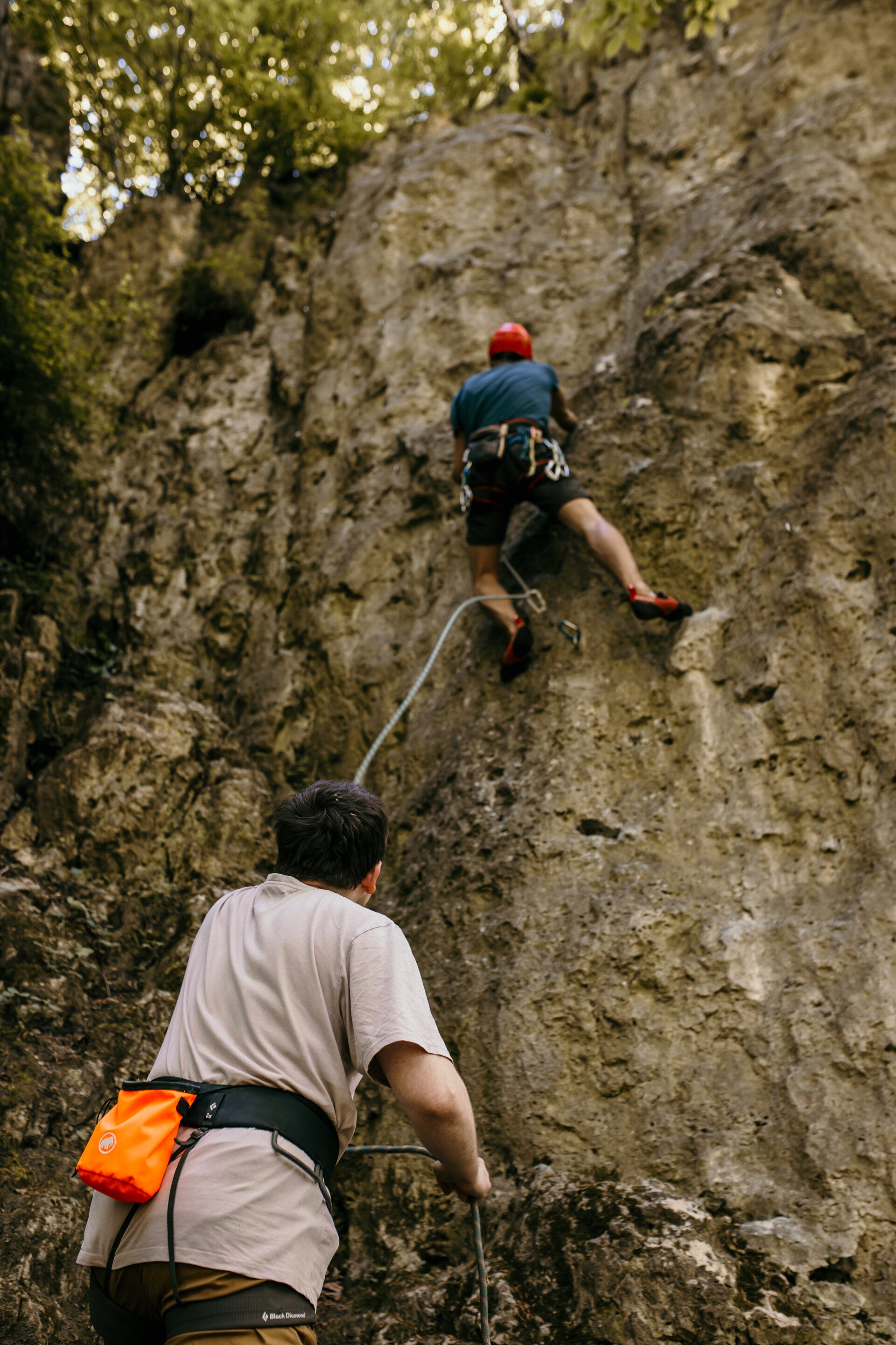 Two people, climber climbing a rock and belayer belaying him