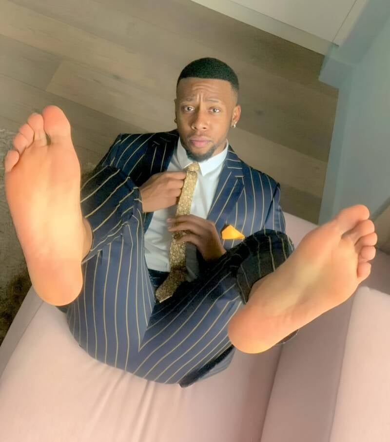 Handsome black guy in suit with legs up as he's laid back on a couch with his bare feet up in the air towards the camera showing off smooth soles and well groomed toes.