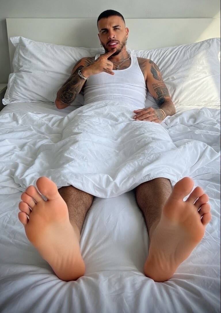 Hot latino laying in bed with his bare feet sticking from under the covers. Showing off smooth soles, long toes, flat feet with no arch.