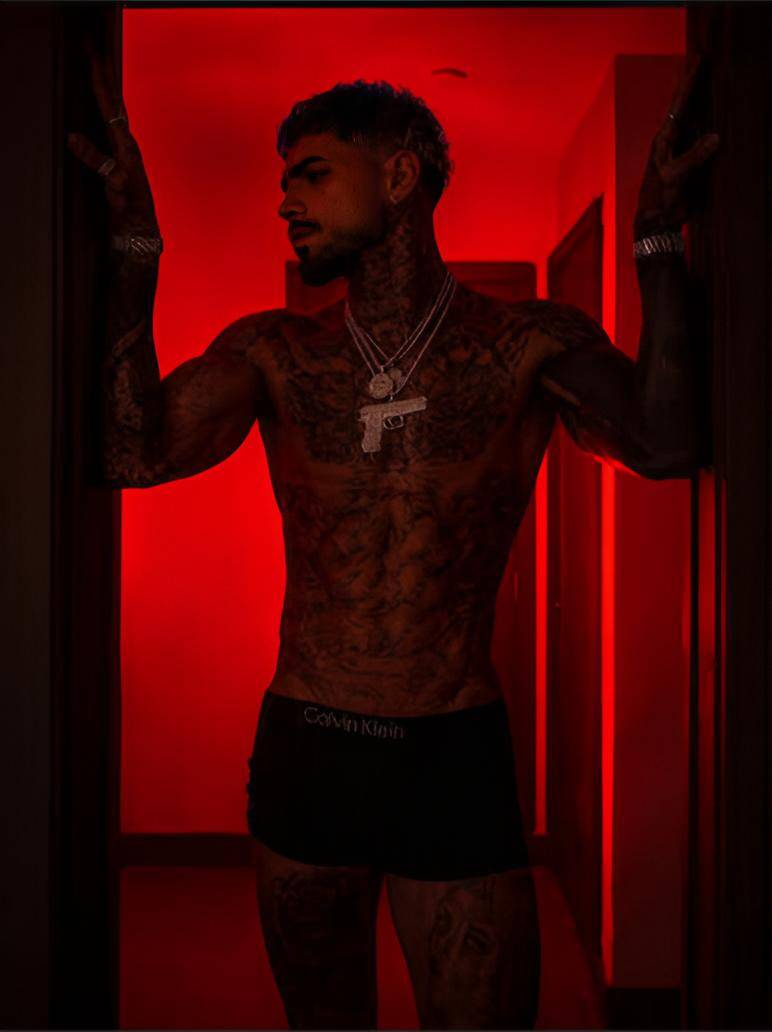 Muscular latino male modeling dark underwear confidently as a red light glows behind him giving him an alluring look.