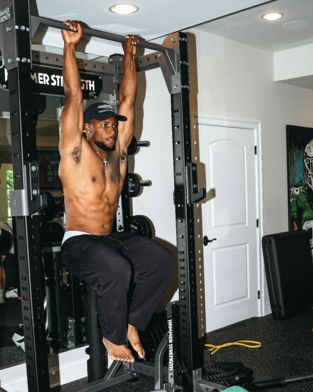 Shirtless Saquon Barkley at home gym doing pullups barefoot with top of his toes showing. 