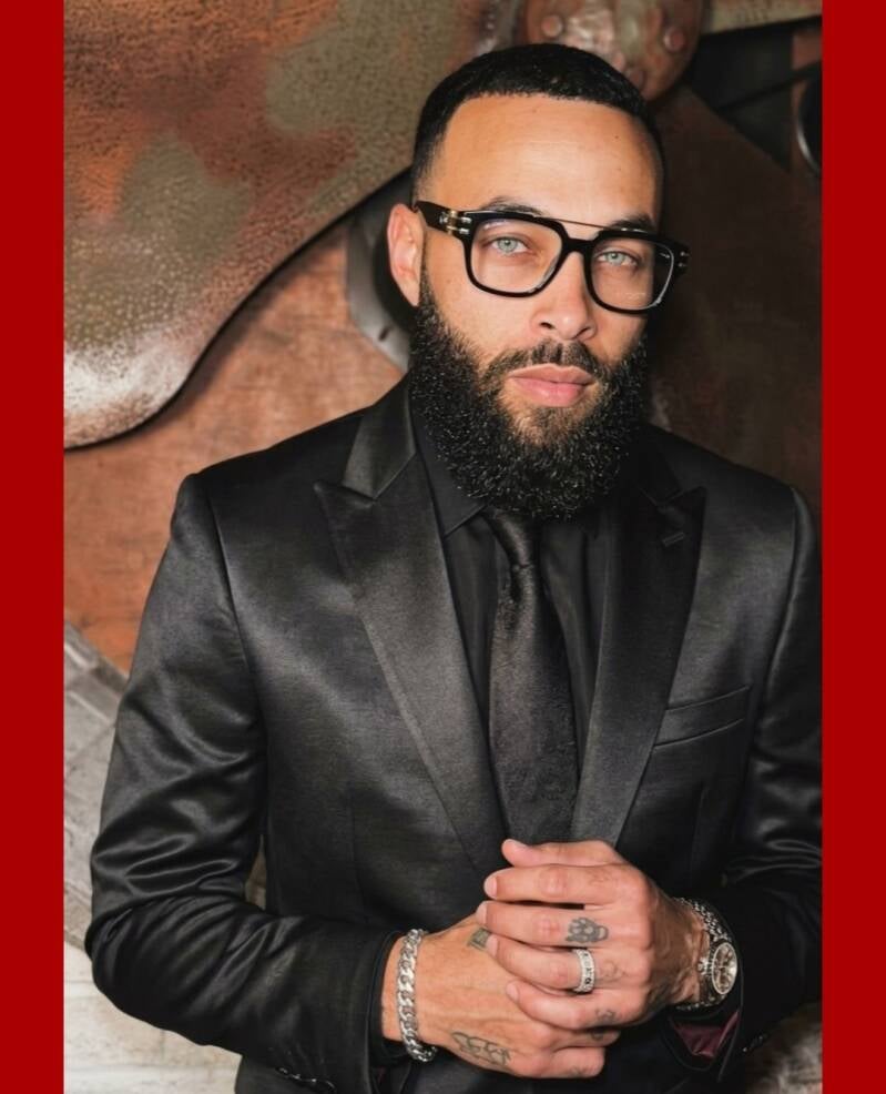 Rickii Samoan light skinned black website owner, and model, in designer glasses, beard, black suit looking bold, and professional.