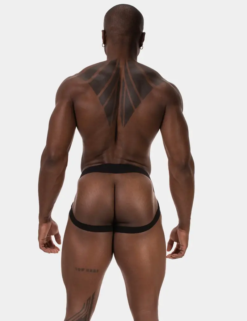 Tattooed muscular bald handsome guy showing off his defined back as he models a black jock strap from the back view.