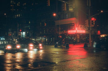 Rue éclairée de nuit avec des phares de voitures et des reflets sur la chaussée
