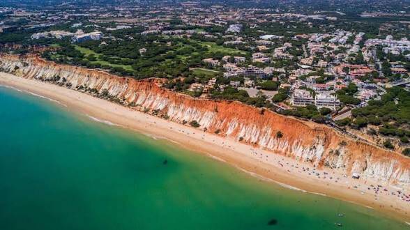 Long sandy beach beneath red and golden cliffs at Praia da Falésia, Algarve.