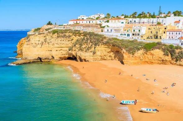 Sandy beach framed by cliffs and white buildings in Carvoeiro, Algarve.