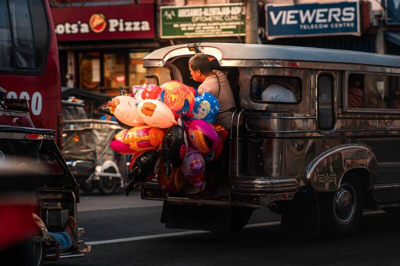 Street scene: A vendor carrying colourful balloons beside a jeepney on a busy city street in the Philippines.