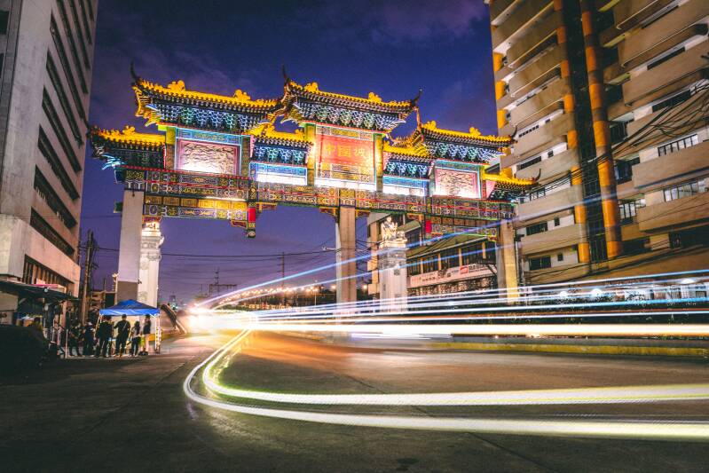 Chinatown gateway: An ornate, brightly lit Chinese-style gateway spans a busy city street at night, with vehicle lights passing beneath