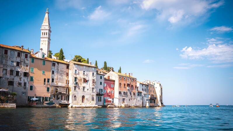 Colourful historic waterfront buildings and a church bell tower overlooking the blue Adriatic Sea in Croatia.