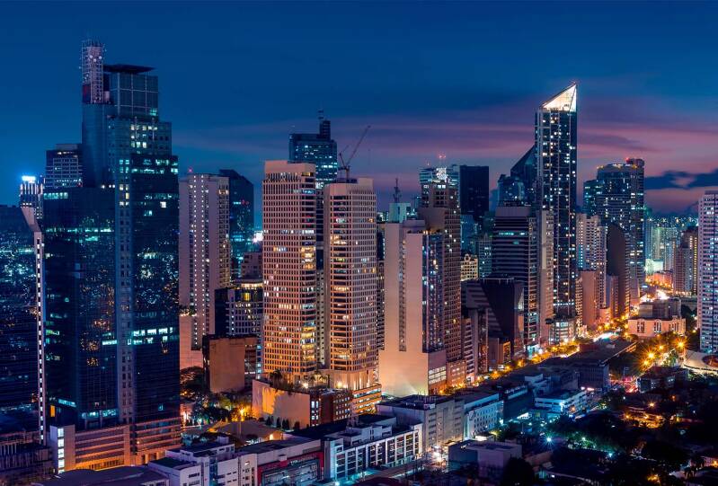 Manila skyline at dusk: High-rise buildings across Manila illuminated against a deep blue and pink evening sky.