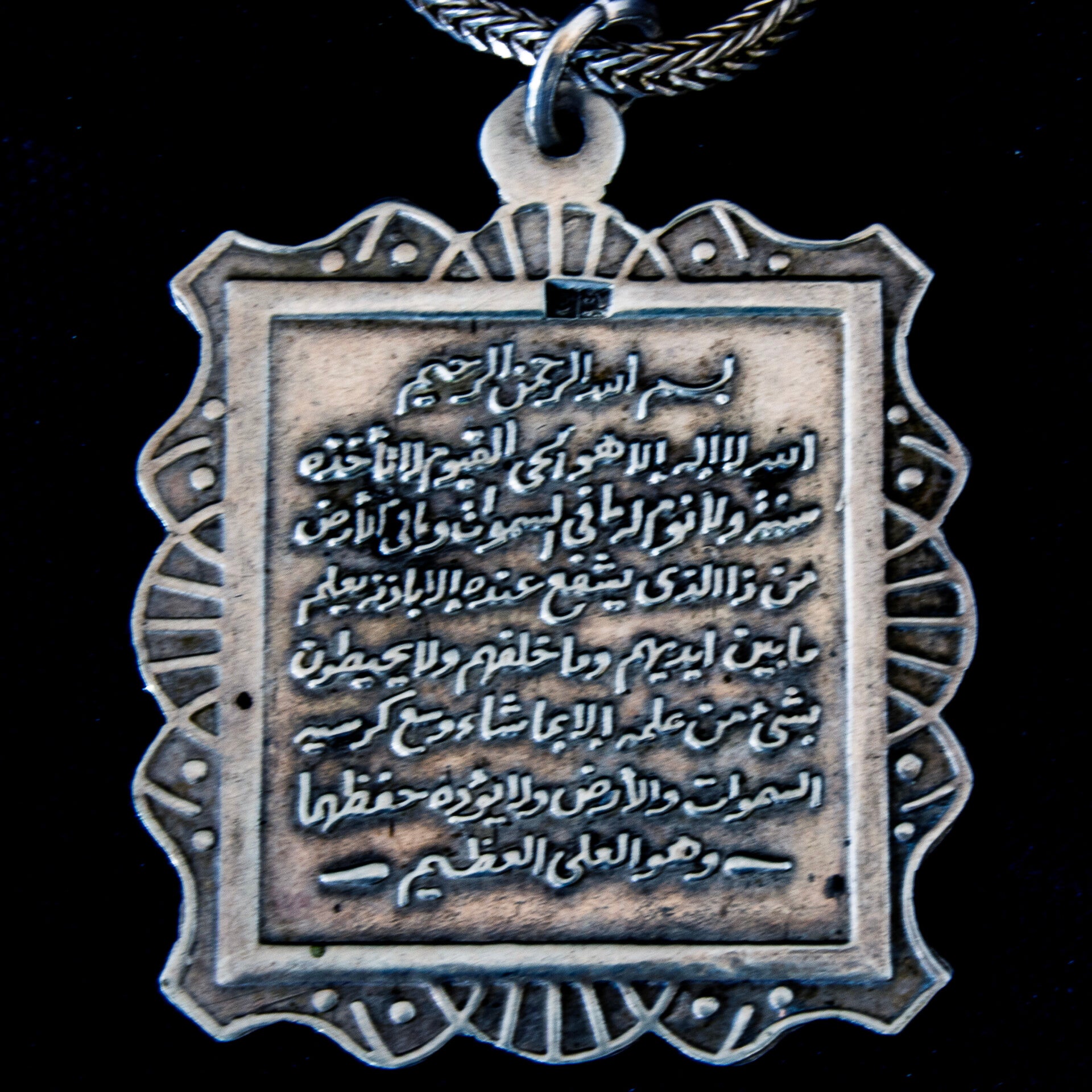 Silver pendant style necklace with a raised letter verse from the Quran