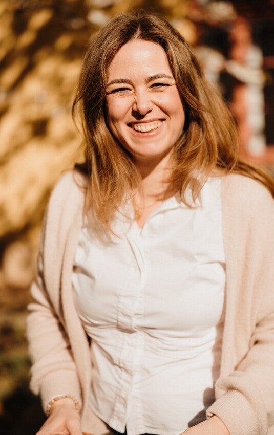 Jennifer Böhnke lächelt herzlich in die Kamera, im Hintergrund unscharfe herbstliche Bäume im warmen Licht.