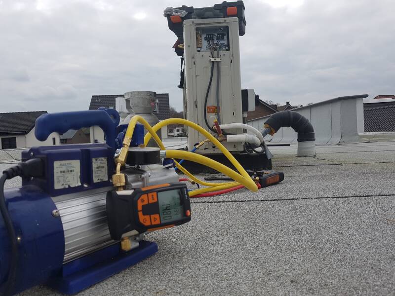 Airco buitendeel op plat dak, vacuumpomp en meterset aangesloten om het systeem te vacumeren.
