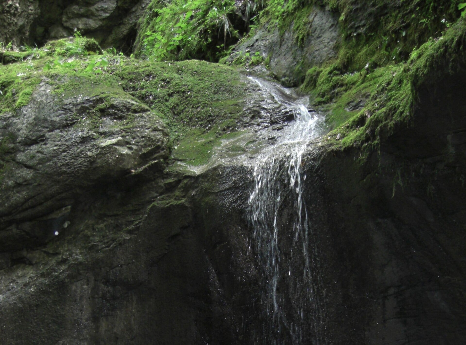 Wasserfall, der über moosbewachsene Steine in einen dunklen Abgrund stürzt