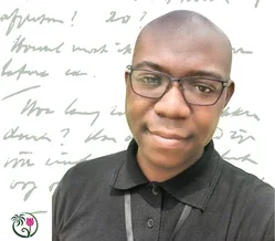 Een jongvolwassen vrouw met lang bruin haar zit buiten op een bank en lglimlacht voor zich uit.