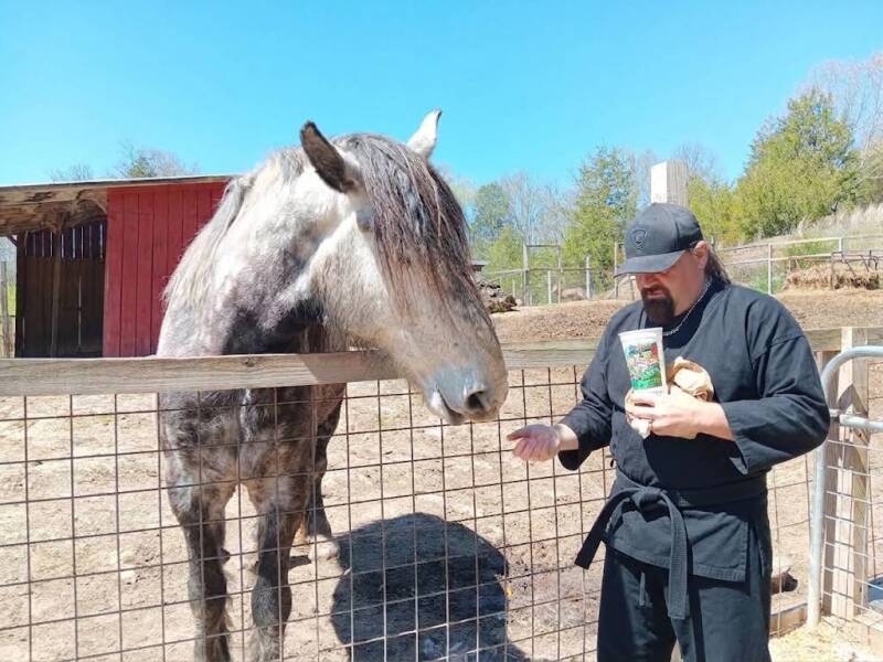 Martial arts instructor Bobby Calvert in his official uniform hand-feeding a horse at the Smoky Mountain Deer Farm in Pigeon Forge, Tennessee.