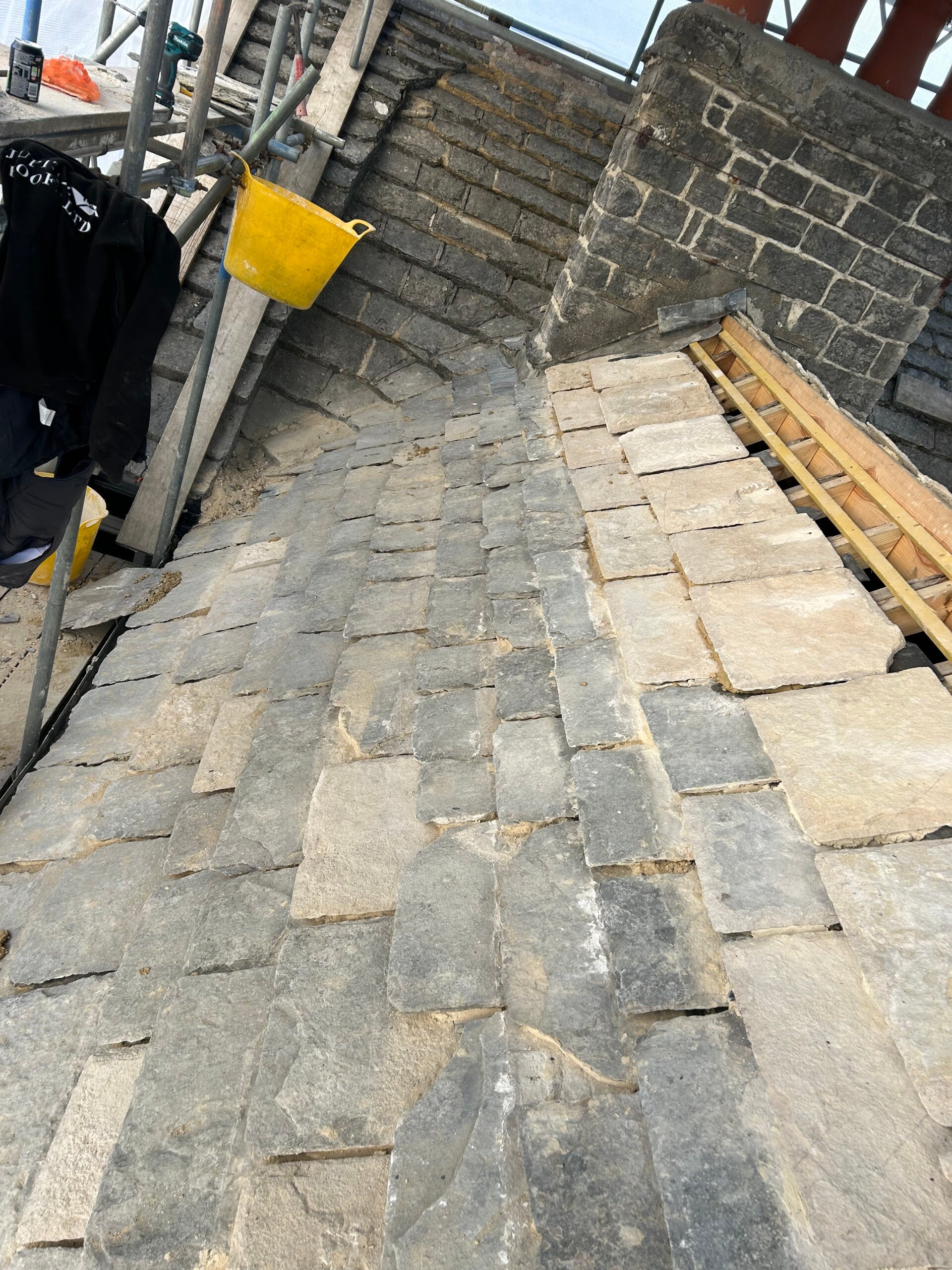 Slate roof under repair with damaged tiles removed, exposing roof battens beneath