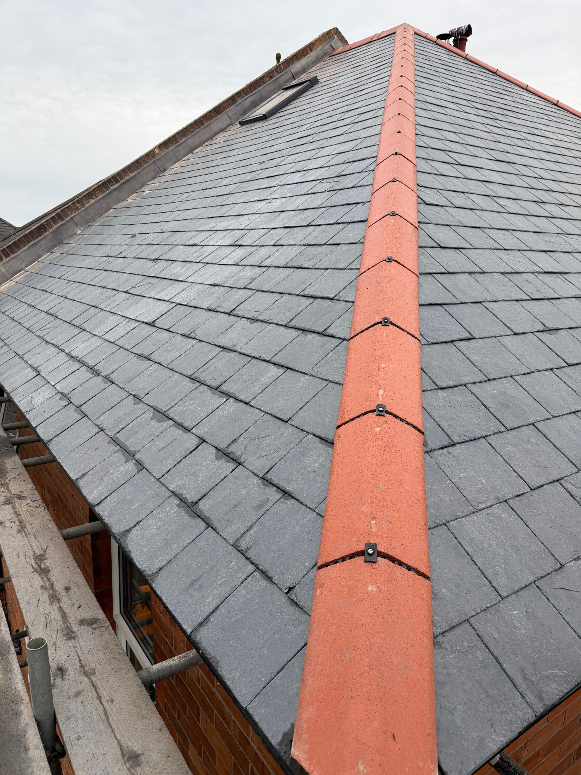 Natural slate roof with red ridge tiles fitted, viewed from ground level during installation