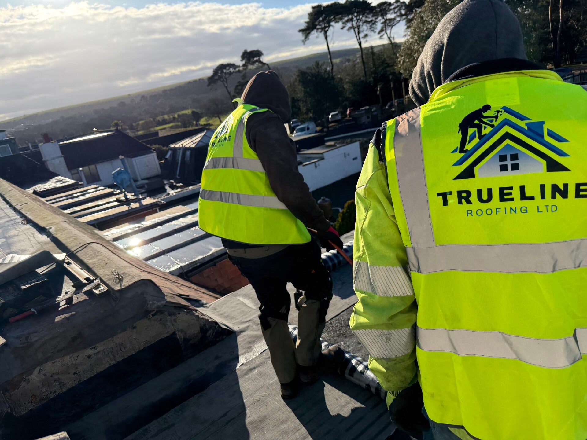 Trueline Roofing Ltd team members working on a roof wearing branded high-visibility jackets during installation work