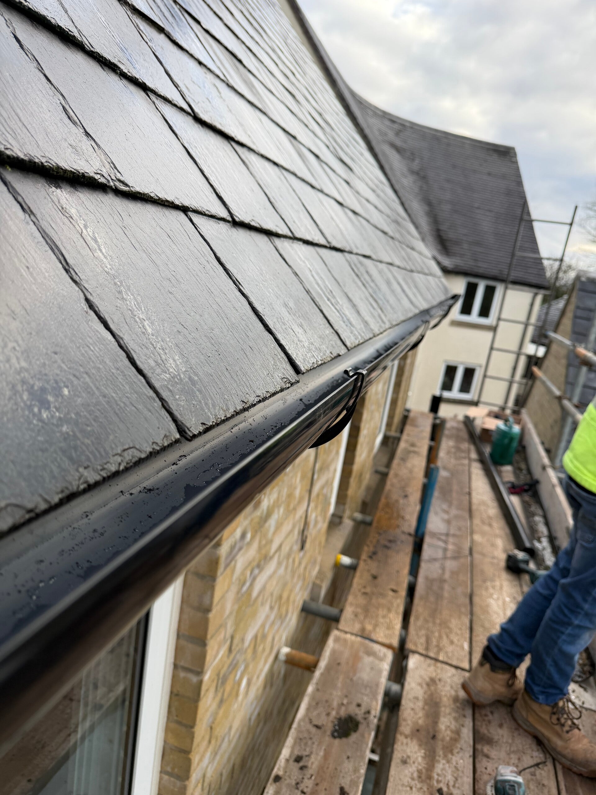 Close-up of slate roof edge with black guttering installed alongside scaffolding