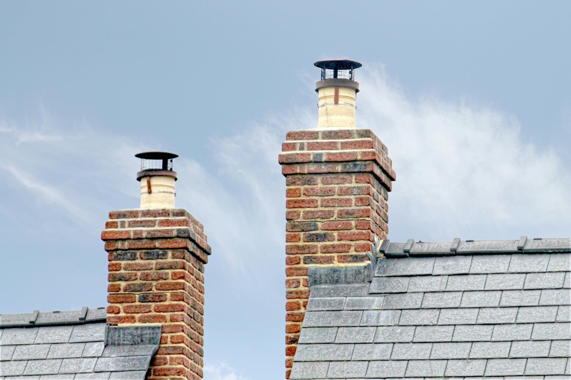 Two roofers carrying out roof repair work on a pitched tiled roof of a residential property under a clear blue sky