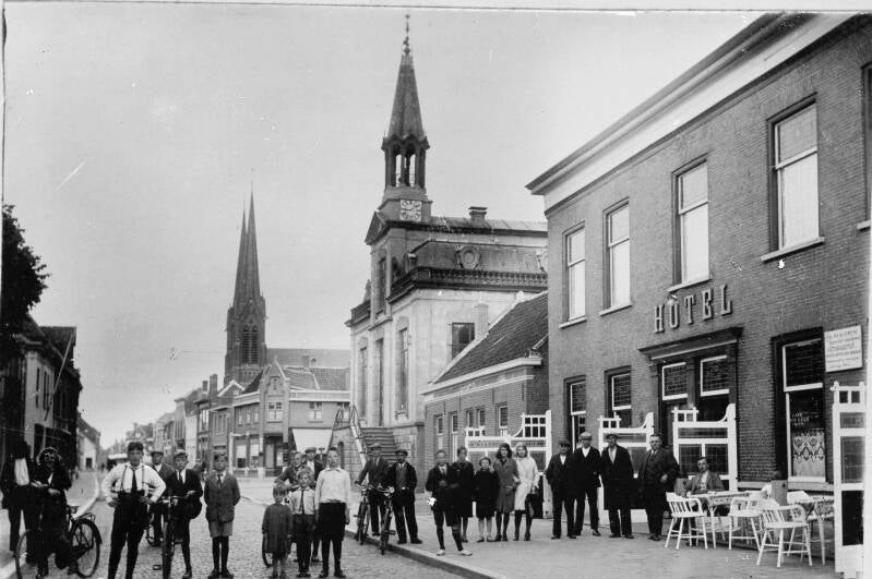 BSK0012 - Bewoners voor Hotel van den Assem, met het gemeentehuis en de St. Jan op de achtergrond, circa 1920.