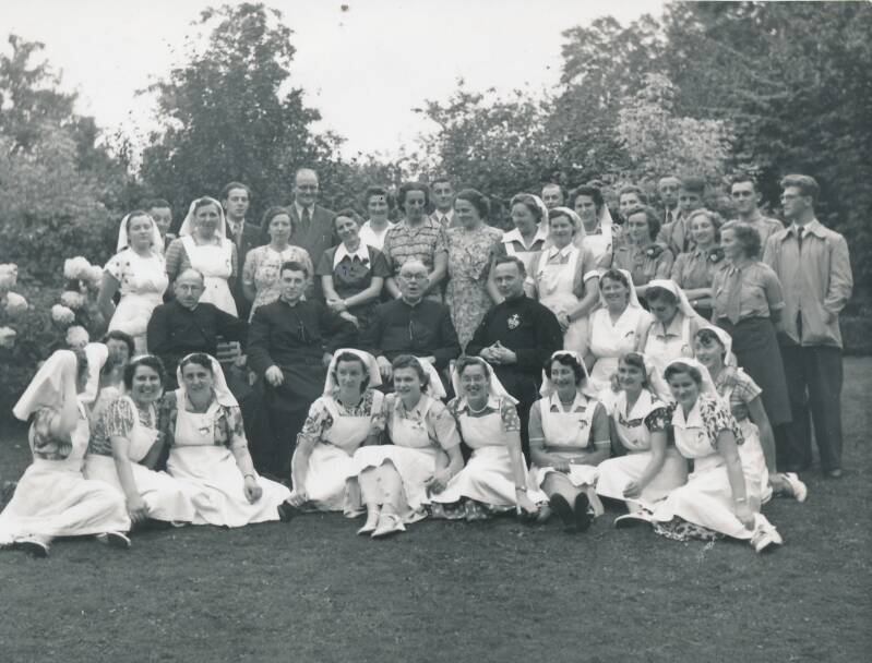 BSK0036 - Een groep, waarschijnlijk in de pastorietuin, met in het midden zittend pastoor Van den Brekel.