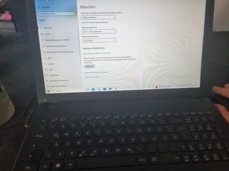 Ein Laptop auf dem Schreibtisch zeigt die Windows 10 Anzeigeeinstellungen für mehrere Bildschirme. Daneben ruht eine Hand neben einer Kaffeetasse.