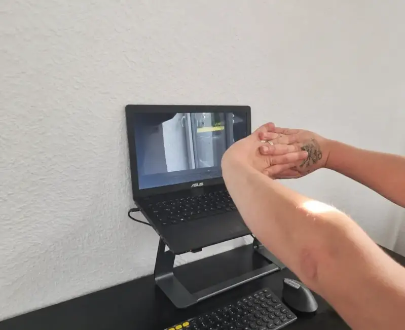 Mann im Homeoffice streckt die Arme am Schreibtisch aus zur Entspannung. Im Vordergrund ein ergonomisches Setup mit Laptopständer, externer Tastatur und vertikaler Maus.