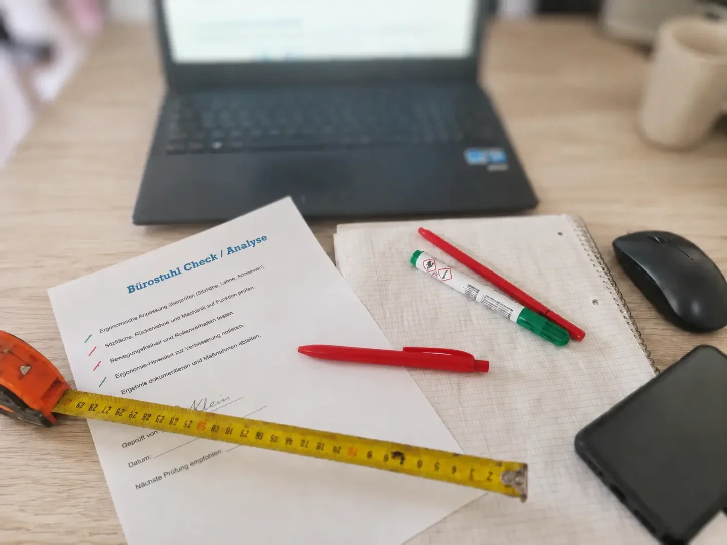 Bürostuhl Ergonomie Check mit Maßband und Checkliste auf dem Schreibtisch.