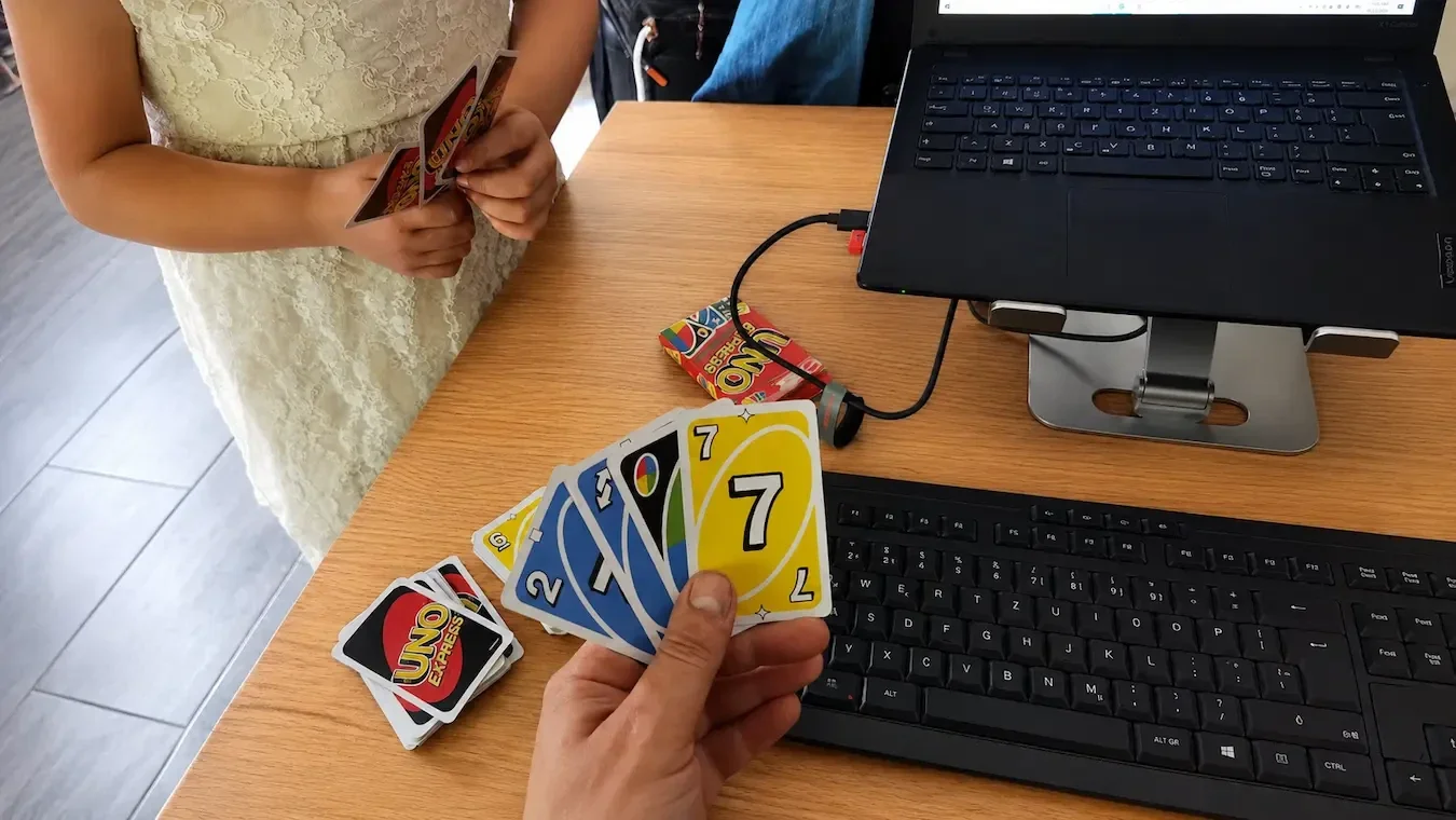 Vater und Tochter spielen während einer Homeoffice-Pause UNO am Esstisch neben Laptop und Tastatur
