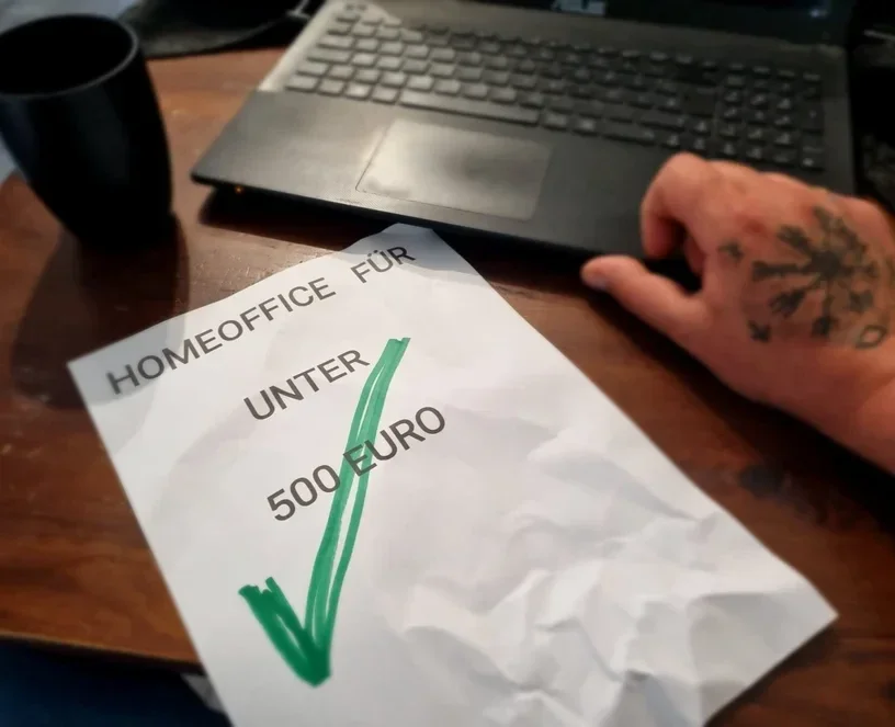 Notiz „Homeoffice für unter 500 Euro“ neben einem Laptop auf Jens’ Schreibtisch