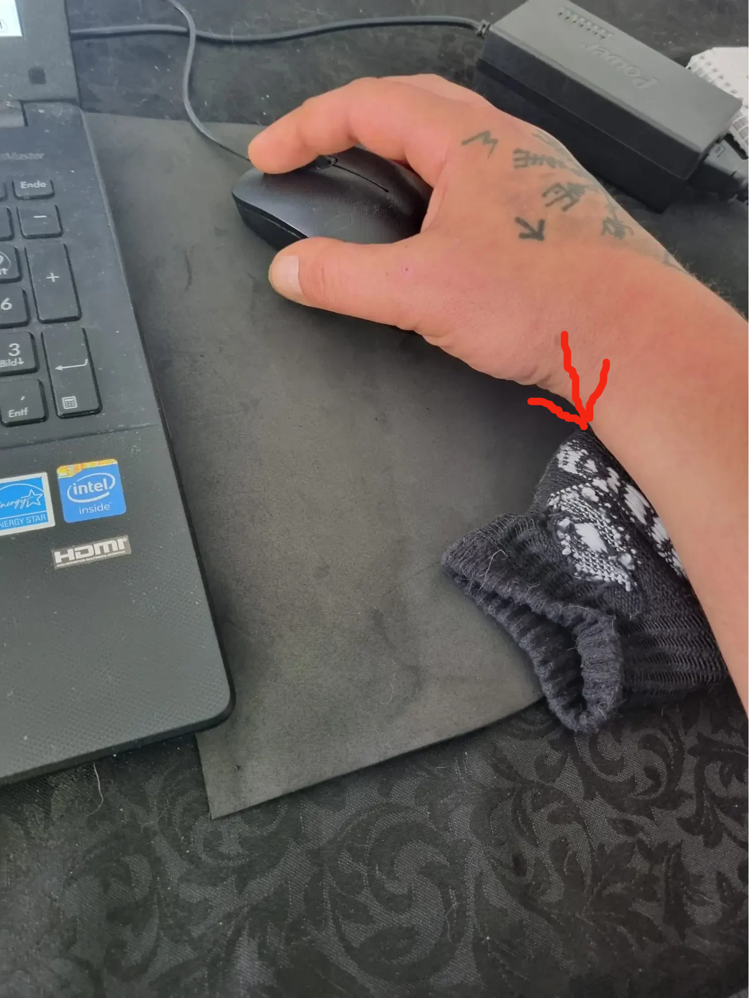 Handballen liegt auf einem gefalteten Tuch vor einer Computermaus zur Entlastung des Handgelenks im Homeoffice.