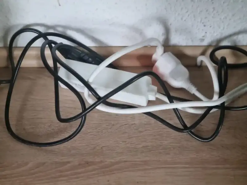 Unordentlicher Kabelsalat aus schwarzen und weißen Stromkabeln an einer Mehrfachsteckdose auf einem Schreibtisch als Beispiel für ungeordnete Technik im Homeoffice.