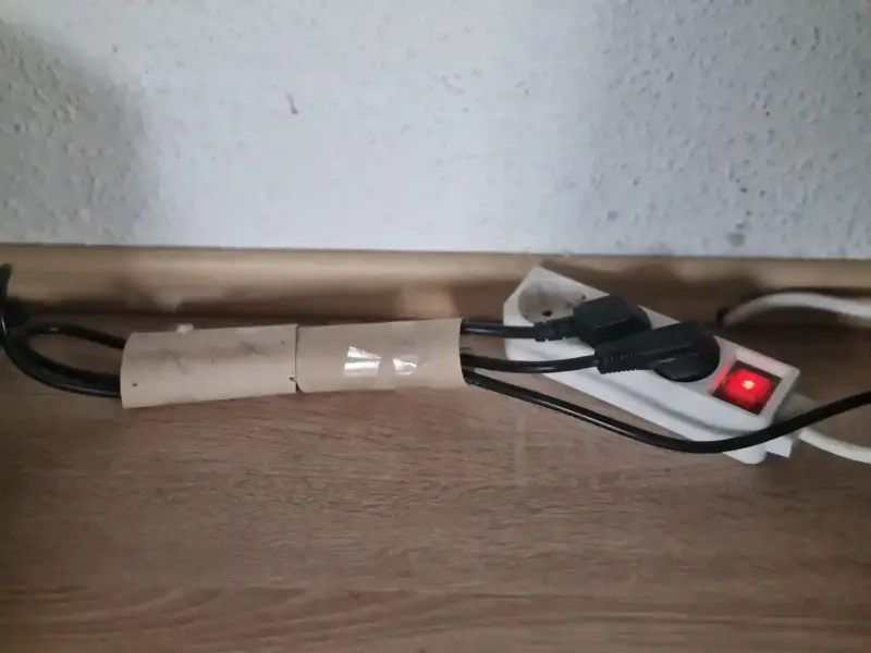 DIY-Lösung für Ordnung am Schreibtisch: Stromkabel wurden mit Hilfe einer Papprolle gebündelt und sauber an die Mehrfachsteckdose geführt, um das Kabelchaos im Homeoffice zu beseitigen.