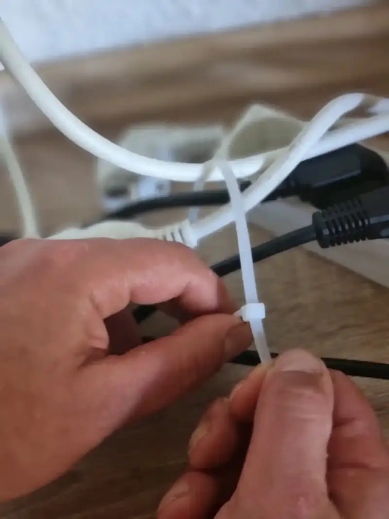 Echtes Praxis-Beispiel: Hände bündeln Schreibtisch-Kabel mit einem weißen Kabelbinder für ein sauberes Kabelmanagement.