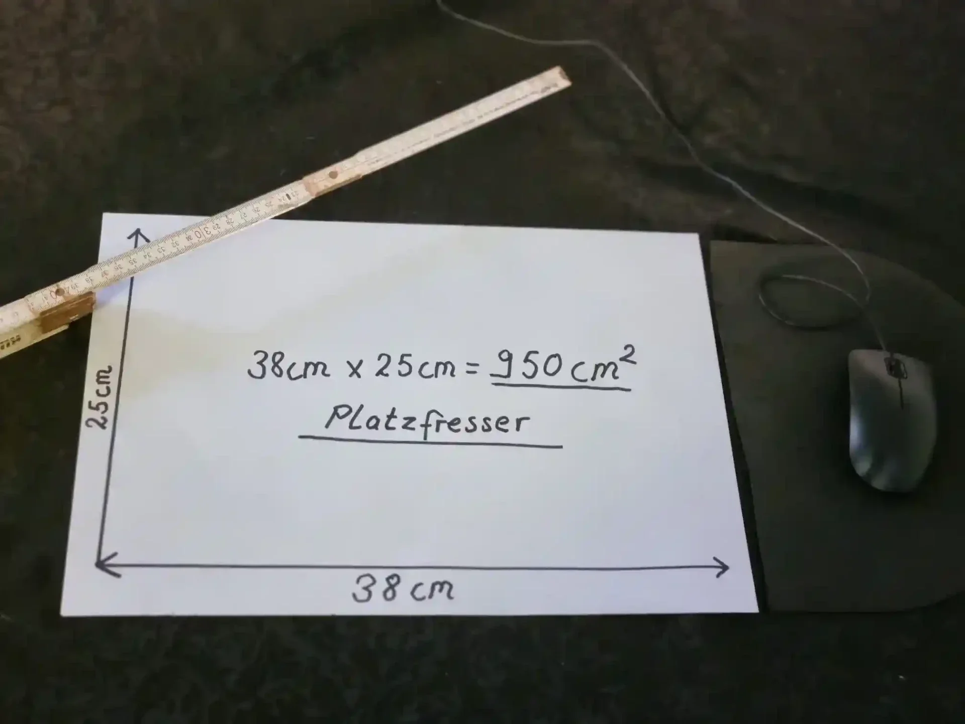 E-E-A-T Praxis-Beweis im Homeoffice: Ein Blatt Papier mit den Maßen 38x25 cm zeigt den enormen Flächenverbrauch eines Laptops. Ein Zollstock und eine Maus verdeutlichen, wie viel wertvolle Arbeitsfläche dieser Platzfresser blockiert.