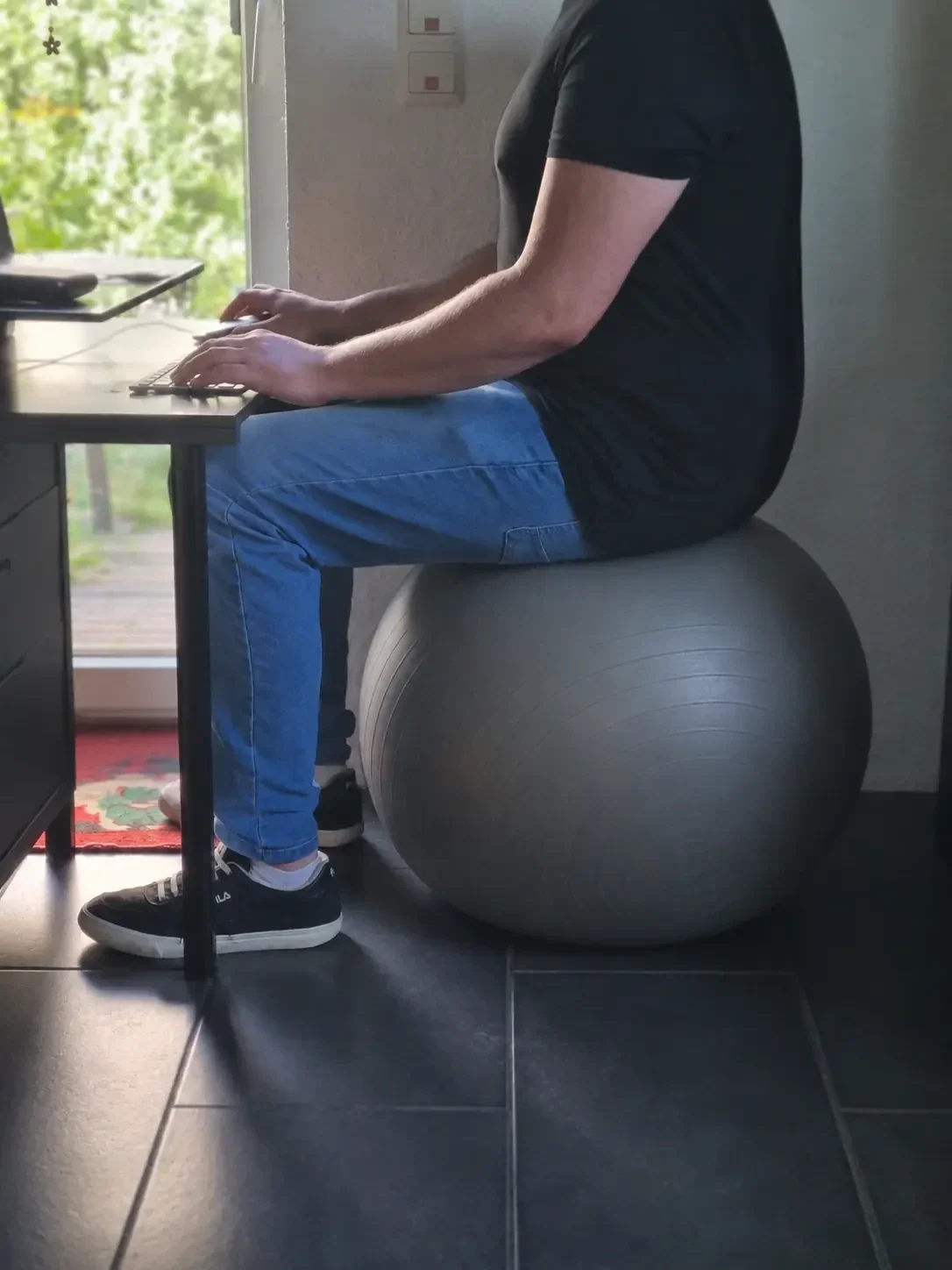 Praxistest im Homeoffice: Ergonomisches Sitzen auf einem grauen Gymnastikball am Schreibtisch mit optimalem Beinwinkel.