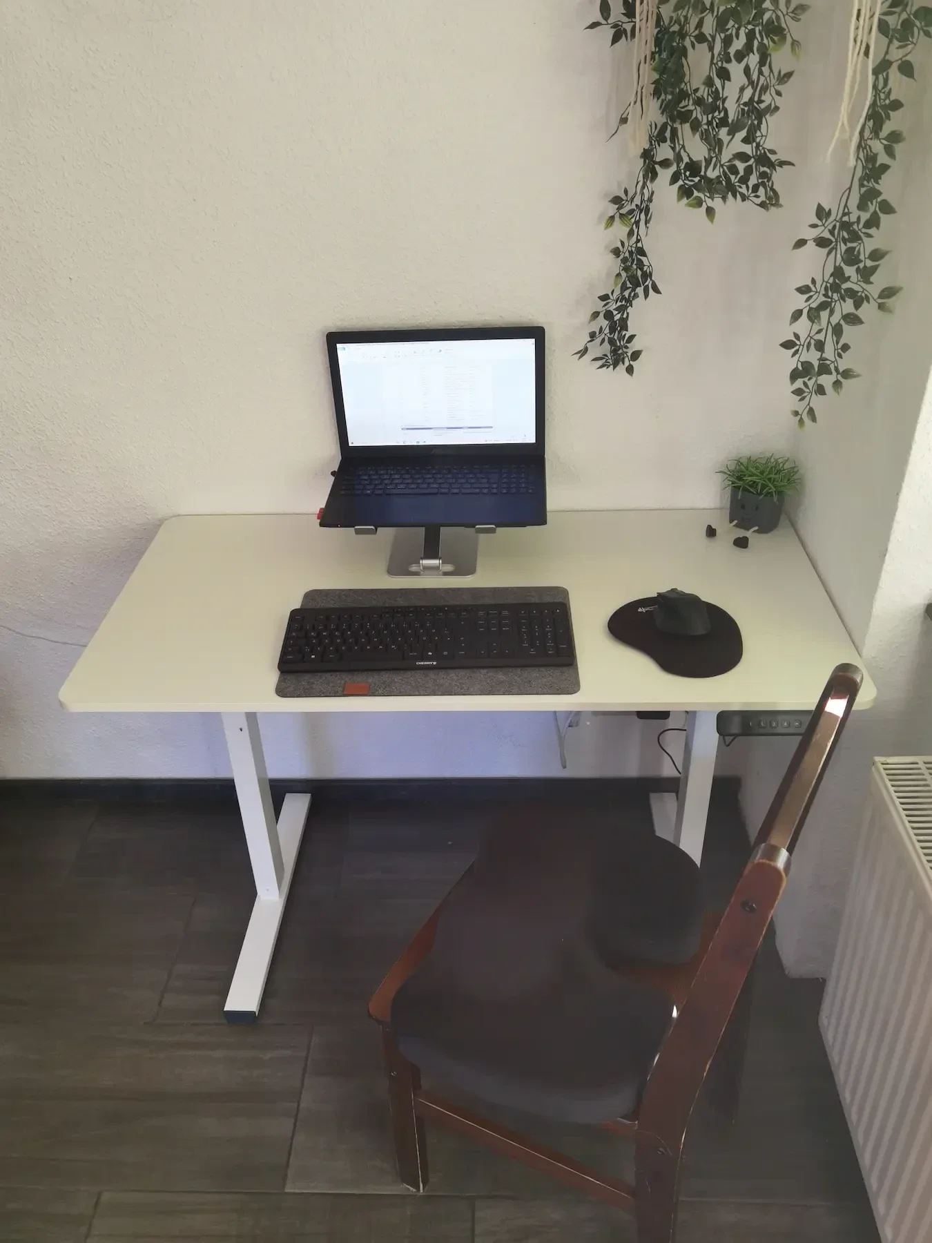 Weißer SANODESK FQ2 mit Laptop auf einem Ständer, externer Tastatur und Maus im Wohnzimmer.
