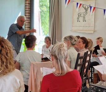 Dirigent Wim Vluggen achter keyboard tijdens repetitie zomer zangweek