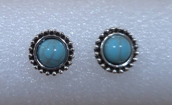 Zilverkleurige ronde oorknopjes met synthetisch turquoise steentjes.