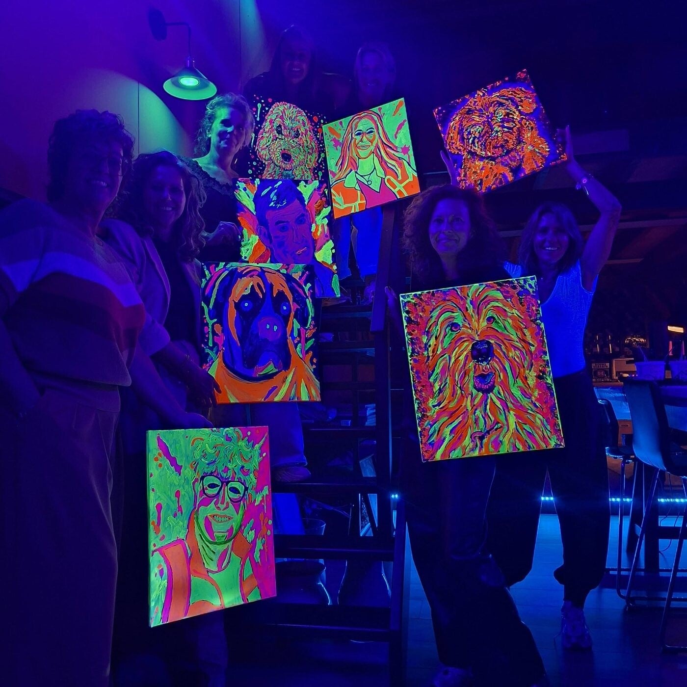 Groep deelnemers toont de zelfgemaakte Neon Pop-Art schilderijen na een workshop bij THILS in Lichtenvoorde.