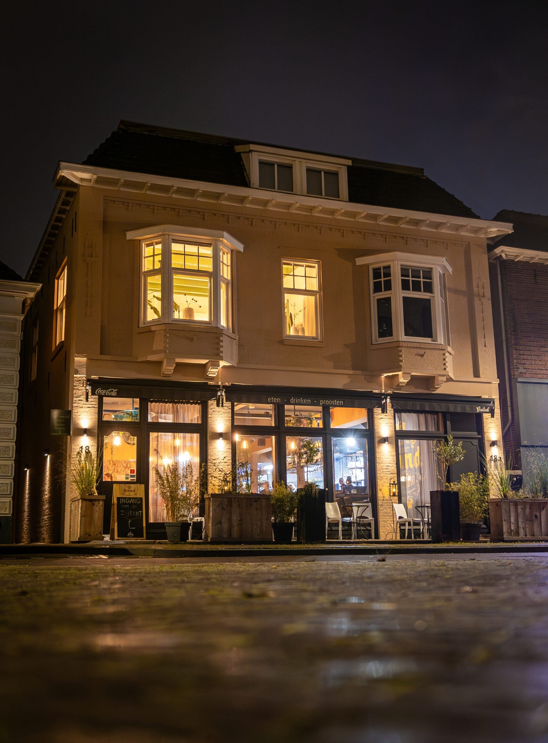 Sfeervol verlichte gevel van restaurant De Oudestraat in Neede bij avond. Samenwerkingslocatie van THILS Workshops & Creaties in de Achterhoek.