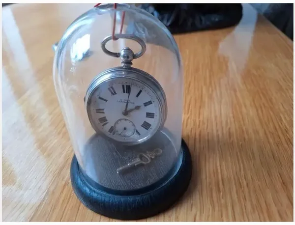 Zakhorloge E.WISE (Manchester). Zilver. Lepine, Half Fusee. Birmingham, 1900 Zilverkleurig Hangt in de stolp aan haakje (op foto met paperclip, waren haakje kwijt. Is inmiddels gevonden) Met sleutel Witte porseleinen wijzerplaat met Romeinse cijfers Met m
