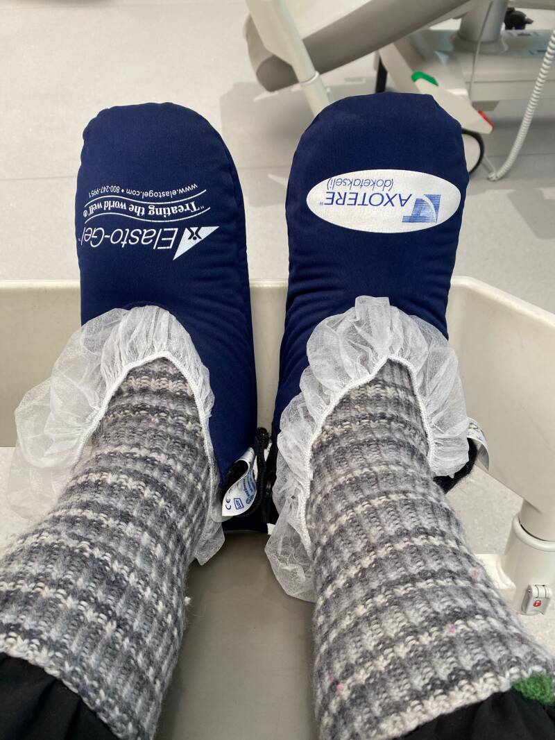 Jalat nilkoista alaspäin, jaloissa villasukat, harsomaiset suojukset ja niiden päällä tummansiniset kylmätossut