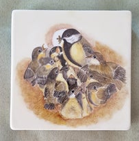 Ein Porzellan-Pfannenuntersetzer zeigt eine Kohlmeise, die ihe Jungen im Nest füttert – liebevoll gestaltet.