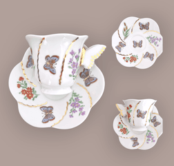 Kundenauftrag – Porzellantasse mit Schmetterlingshenkel und Goldverzierungen auf einem blütenförmigen Unterteller; verziert mit Blumen und sieben Schmetterlingen – drei auf der Tasse, vier auf dem Unterteller.