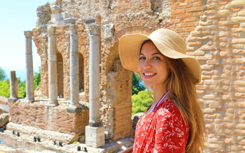 Portrait of young smiling woman with hat in famous Taormina Greek Theatre, Sicily, Italy