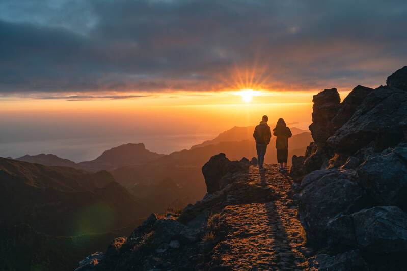 Happy young couple watching sunrise from the peak od Pico do Arieiro in Madeira. Silhouette of couple on the mountains. 
